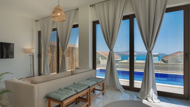 Ein modernes Wohnzimmer mit einer Couch, einer Holzbank, einem Fernseher und großen Fenstern mit Blick auf einen Pool.