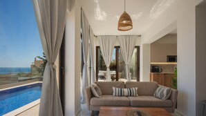 Ein modernes Wohnzimmer mit Sofa, Couchtisch und Blick auf Pool und Meer.