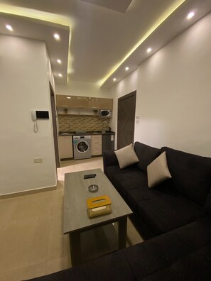A modern living room with a sofa, a coffee table, and a kitchen area in the background.