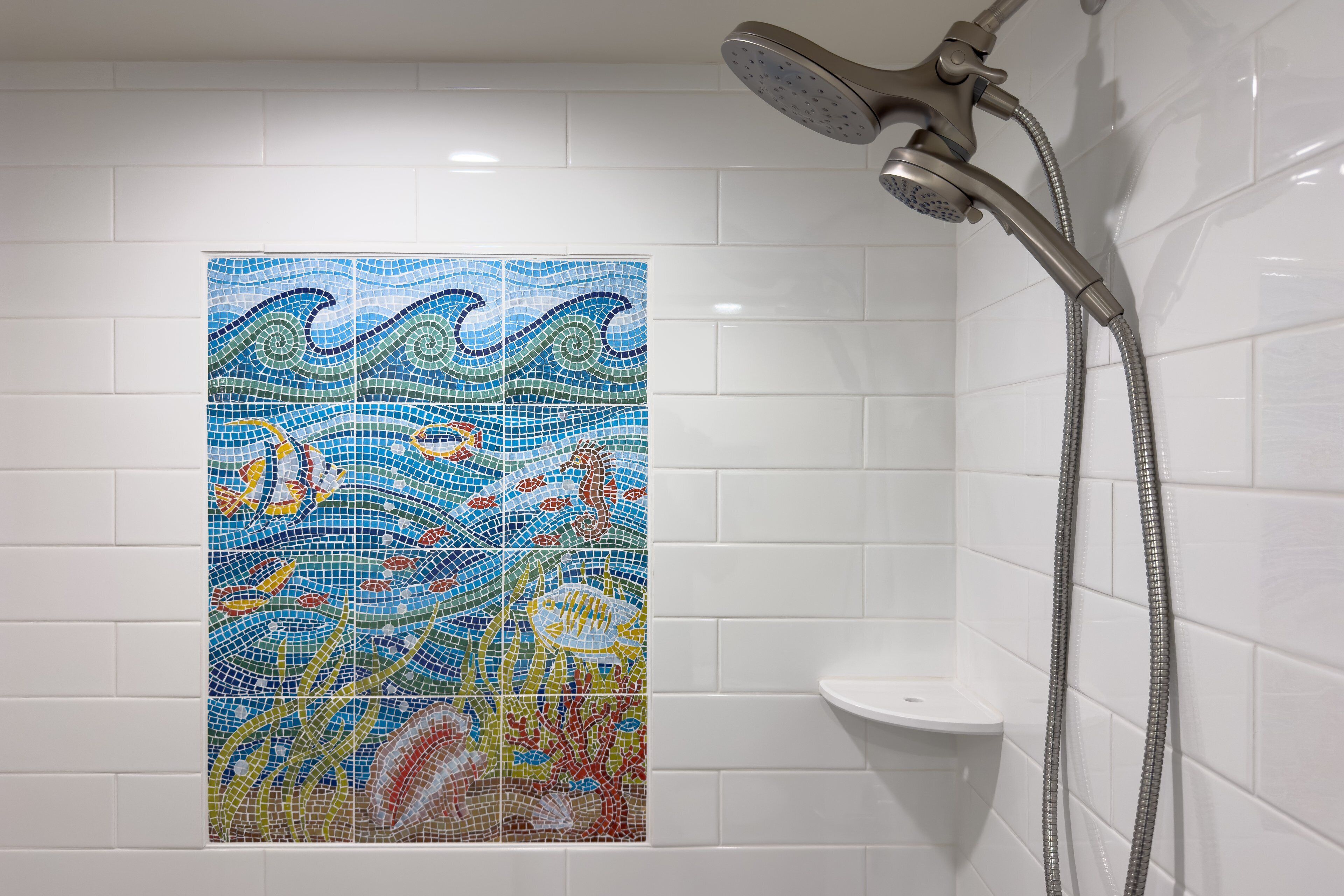 Een badkamer met een mozaïektegel muur waarop zeewezens afgebeeld zijn, een douchekop en een wit wastafel.