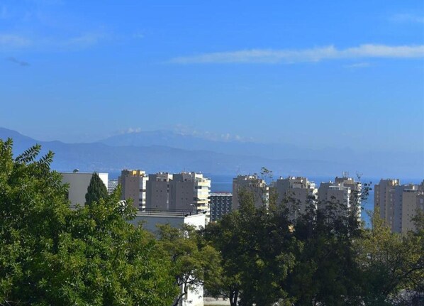 A coastal cityscape with high-rise buildings, a clear sky, and distant mountains.