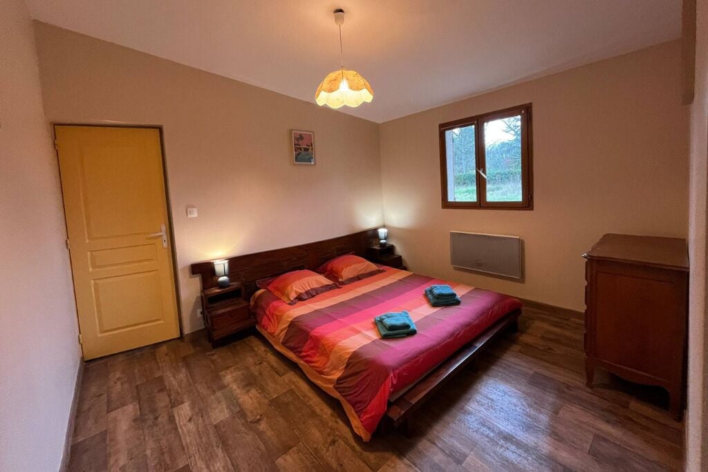 Un dormitorio con cama, mesitas de noche, una ventana y una puerta.