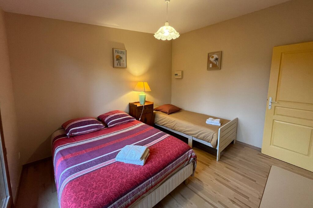 Un dormitorio con una cama grande, una cama más pequeña, una mesita de noche con una lámpara y una puerta.
