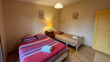 Un dormitorio con una cama grande, una cama más pequeña, una mesita de noche con una lámpara y una puerta.