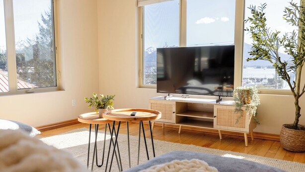 Ein modernes Wohnzimmer mit großem Fernseher, Holzmöbeln und Bergblick durch die Fenster.