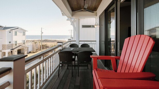 Un balcon doté d’un plafond en bois, d’une chaise rouge et d’une table avec des chaises.