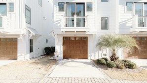 Un bâtiment blanc à deux étages, doté d’une entrée centrale, d’une porte de garage en bois et d’un petit palmier dans le jardin.