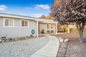 A single-story house with a covered porch, a gravel driveway, and a tree with autumn leaves. - Game room & Fire Pit, Short Walk to Downtown! (Paso Robles)