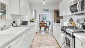 A modern kitchen with white cabinetry, a gas stove, a microwave, and a dining area with a table and chairs. - Game room & Fire Pit, Close to Downtown! (Paso Robles)