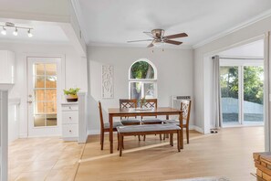 A dining area with a wooden table and chairs, a ceiling fan, and a view through a large window. - Game room & Fire Pit, Short Walk to Downtown! (Paso Robles)