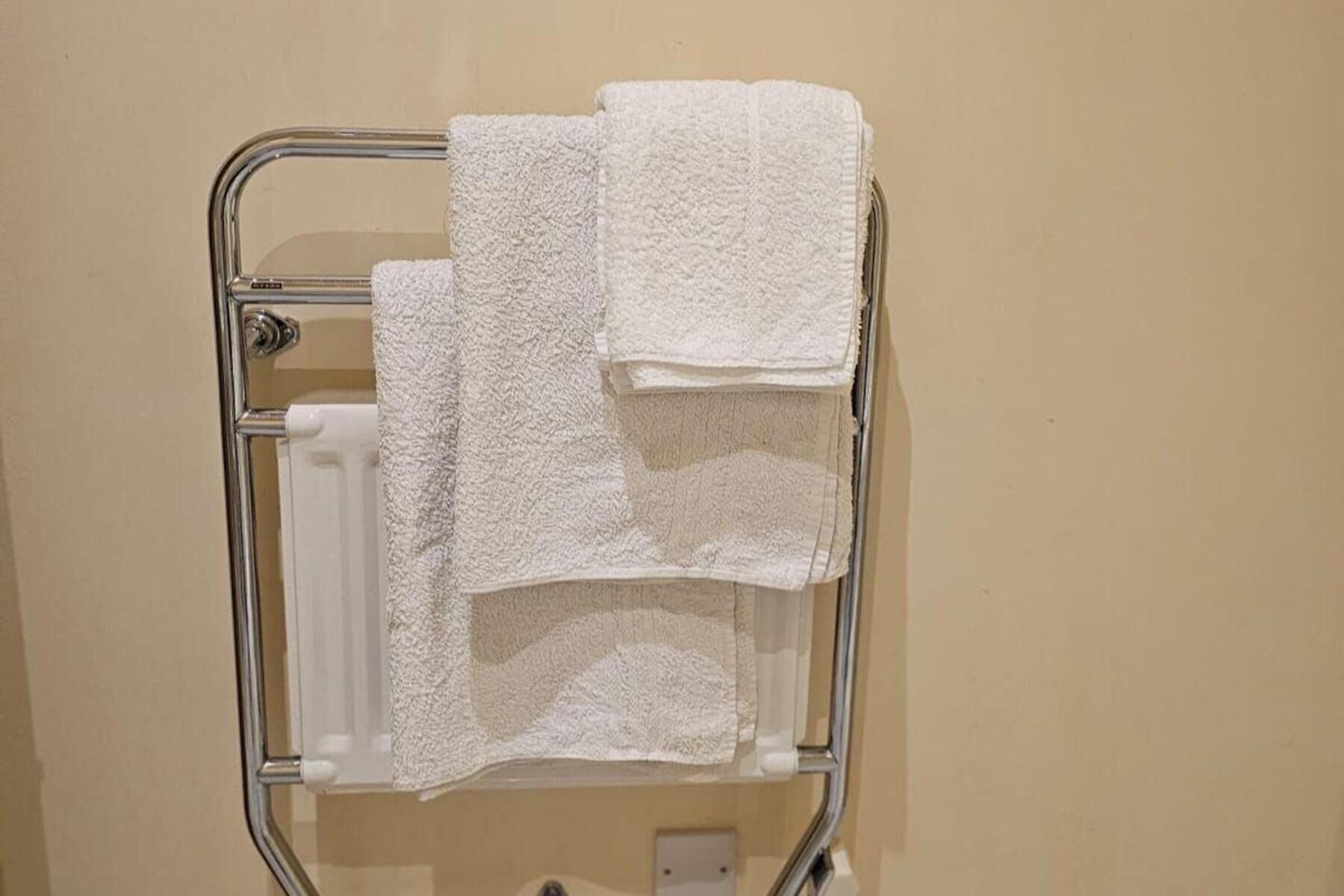 A metal towel rack with three white towels against a beige wall.