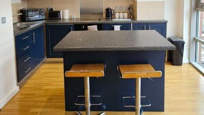 Une cuisine moderne avec des meubles de couleur bleu foncé, un plan de travail en granit et deux tabourets de bar.