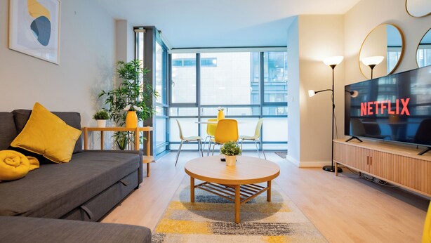 Ein modernes Wohnzimmer mit einer Couch, einem runden Couchtisch und einem Fernseher, der 'NETFLIX' anzeigt.
