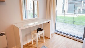 Ein modernes Zimmer mit Glastür zum Balkon, einem weißen Schreibtisch mit Stuhl und einem kleinen Hocker.