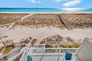 Une vue sur la plage avec une terrasse en bois et une clôture blanche.