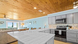 A modern kitchen with a central island, grey cabinets, stainless steel appliances, and a wooden ceiling.