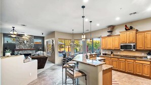 A modern kitchen with wooden cabinets, a central island with bar stools, and a stone fireplace. - 5BR, Pool, Patio, Outdoor TV & In-Pool Hoops (Scottsdale)