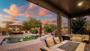 A covered outdoor area with a pool, lounge chairs, and a table with chairs. - 5BR, Pool, Patio, Outdoor TV & In-Pool Hoops (Scottsdale)
