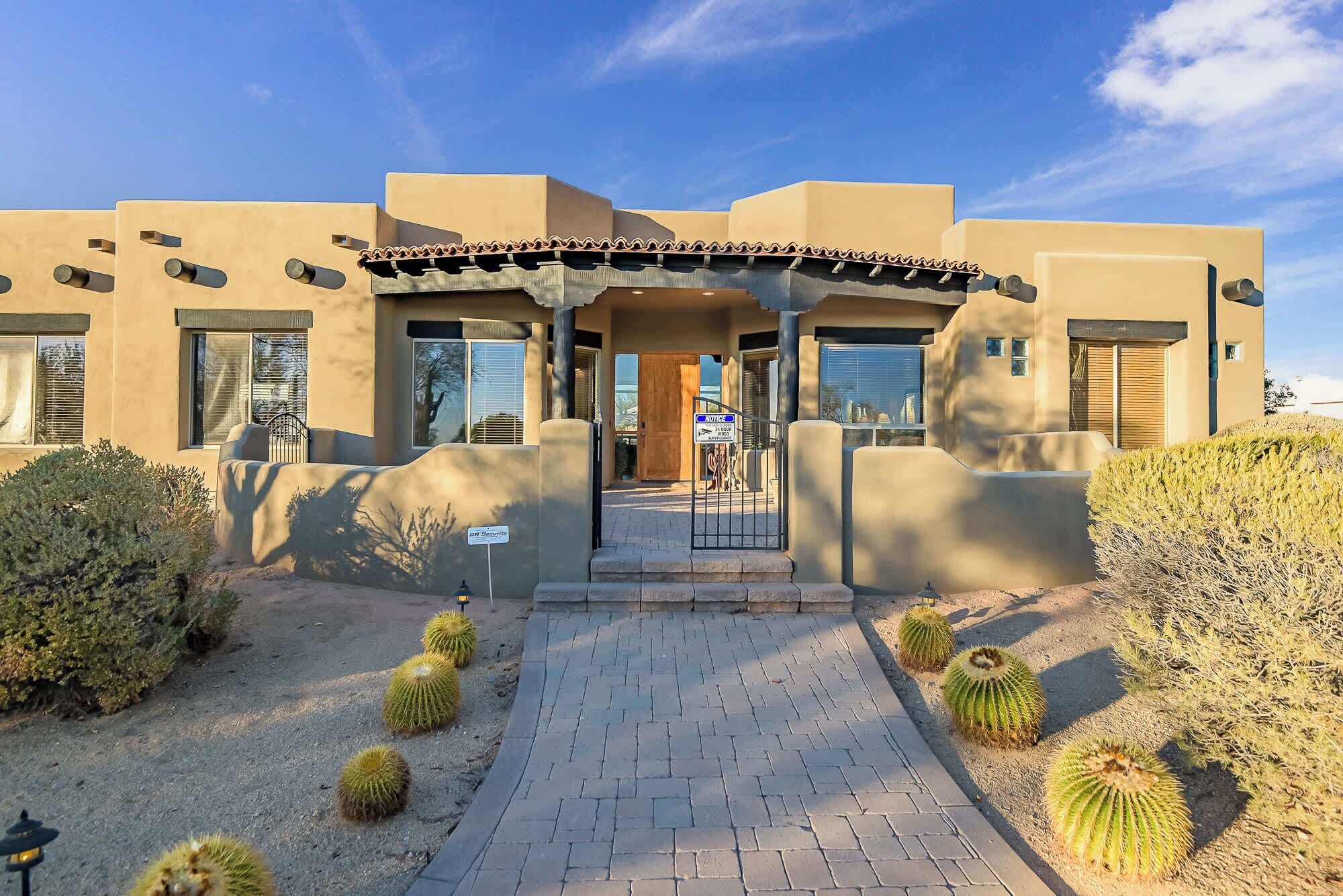 A modern building with a paved entrance, security sign, and cacti landscaping.