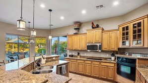 A modern kitchen with granite countertops, wooden cabinets, a stainless steel sink, a microwave, and an oven. - 5BR, Pool, Patio, Outdoor TV & In-Pool Hoops (Scottsdale)