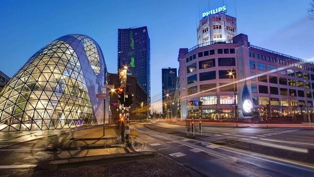 Un paisaje urbano moderno con una estructura geodésica distintiva, un rascacielos con un letrero Philips y un edificio de varios pisos con señalización iluminada.