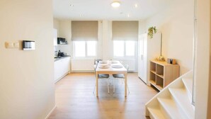 Una cocina luminosa y moderna con armarios blancos, una mesa de comedor con sillas y una escalera que sube a un nivel superior.