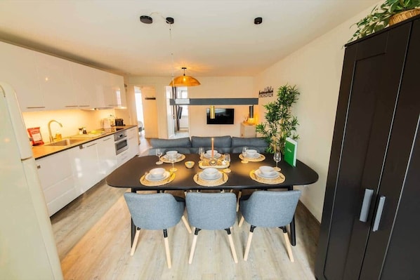 A modern kitchen with white cabinets, a dining table set for six, and a dark-colored cabinet to the right.