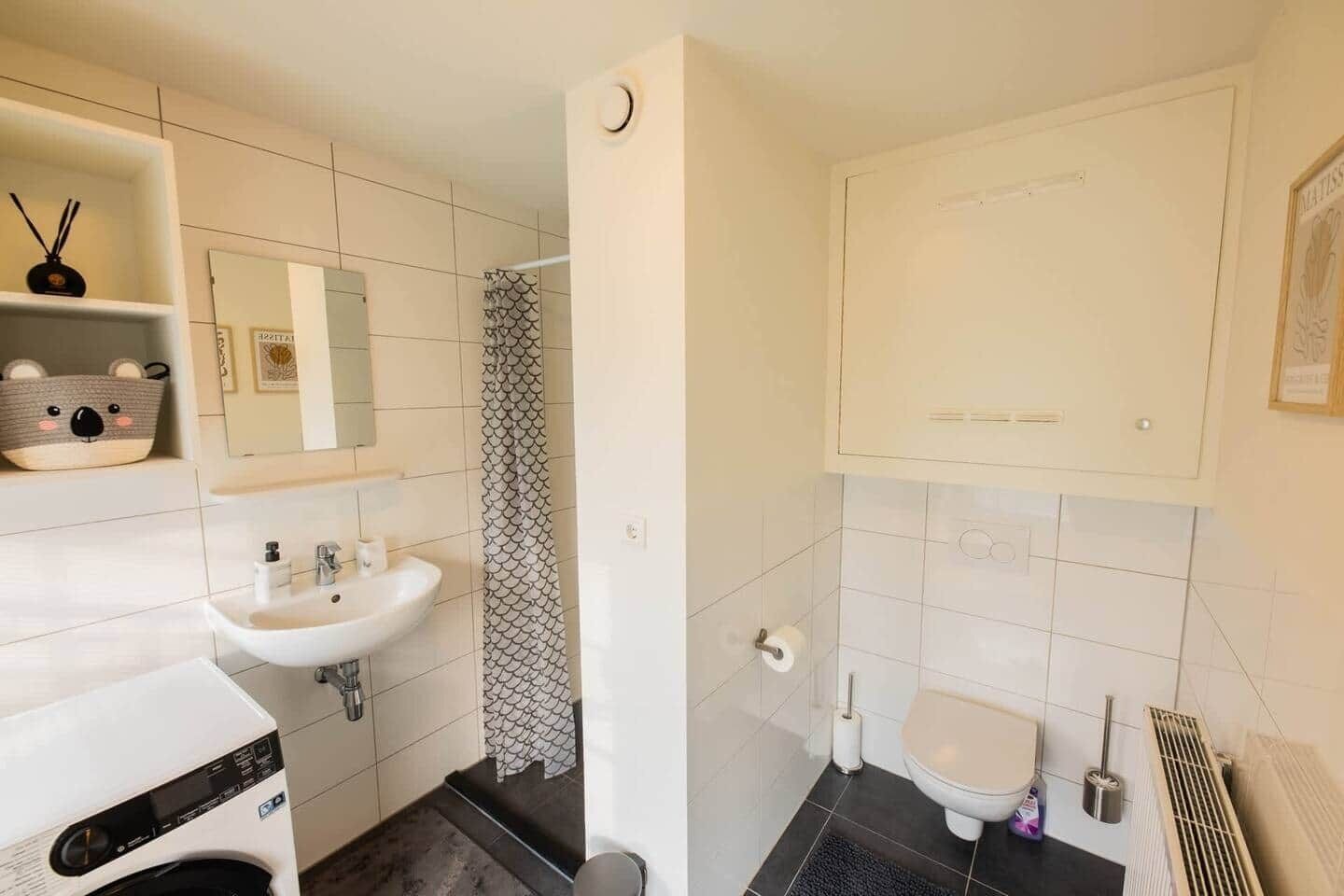 Et badeværelse med vask, toilet, bruser og et spejl.