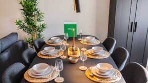 Une table à manger dressée avec de l’assiette blanche, des bols à bord doré et des verres, entourée de chaises noires.