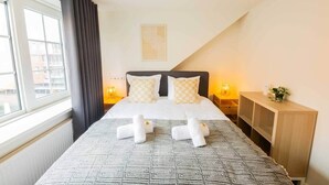 Une chambre d’hôtel comprenant un lit, des lampes de chevet, une table de chevet, une fenêtre avec des rideaux et une vue sur les bâtiments environnants.