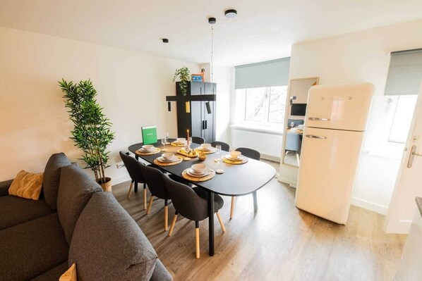 A compact living space with a dining area, a sofa, a refrigerator, and a potted plant.