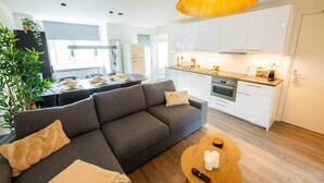 Un salon moderne comprenant un canapé, une table à manger et un coin cuisine avec des meubles blancs et un fourneau.