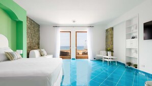 Une chambre à coucher avec un lit, une petite table, une chaise et une vue sur la mer, visible à travers une porte vitrée.