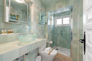 A bathroom with a glass bowl sink, a toilet with a decorative tile, a shower enclosure, and a mirror with a decorative frame. - Stay U-nique Apartments Goya II (Rincon de la Victoria)