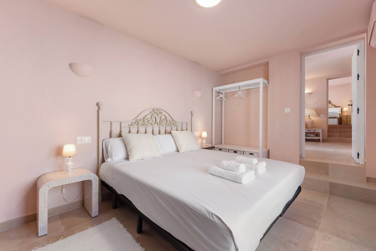 Egy hálószoba, amelyben egy nagy ágy, éjjeliszekrények, baldachinos ágy található, és kilátás nyílik egy másik szobára.