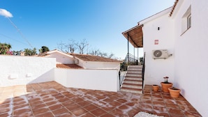 Ein Innenhof mit Terrakottafliesen, einer weißen Wand, einer Treppe und Kübelpflanzen.