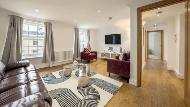 A modern living room with a leather sofa, a red armchair, a glass coffee table, and a large TV.
