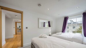 A hotel room with two beds, a mirror, a window with purple curtains, and a view of a building outside.