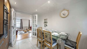 A modern kitchen with wooden cabinets, a glass dining table, and a wall-mounted clock.