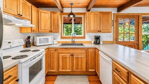 A kitchen with wooden cabinets, a white stove, a microwave, and a coffee maker. - Riverhouse 3 Bedroom Home (Leavenworth)