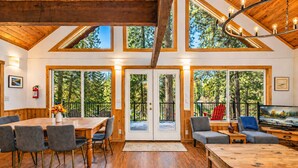 A spacious room with a wooden ceiling, large windows, a dining area, and a seating area with a television. - Riverhouse 3 Bedroom Home (Leavenworth)