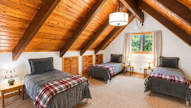 Ein Zimmer mit zwei Betten, Holzbalken, einem Vorhangfenster und einer Lampe auf einem Nachttisch.