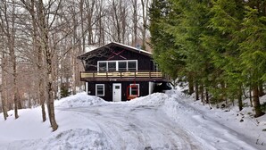 Uma cabana com fachada de madeira, varanda e entrada coberta de neve.