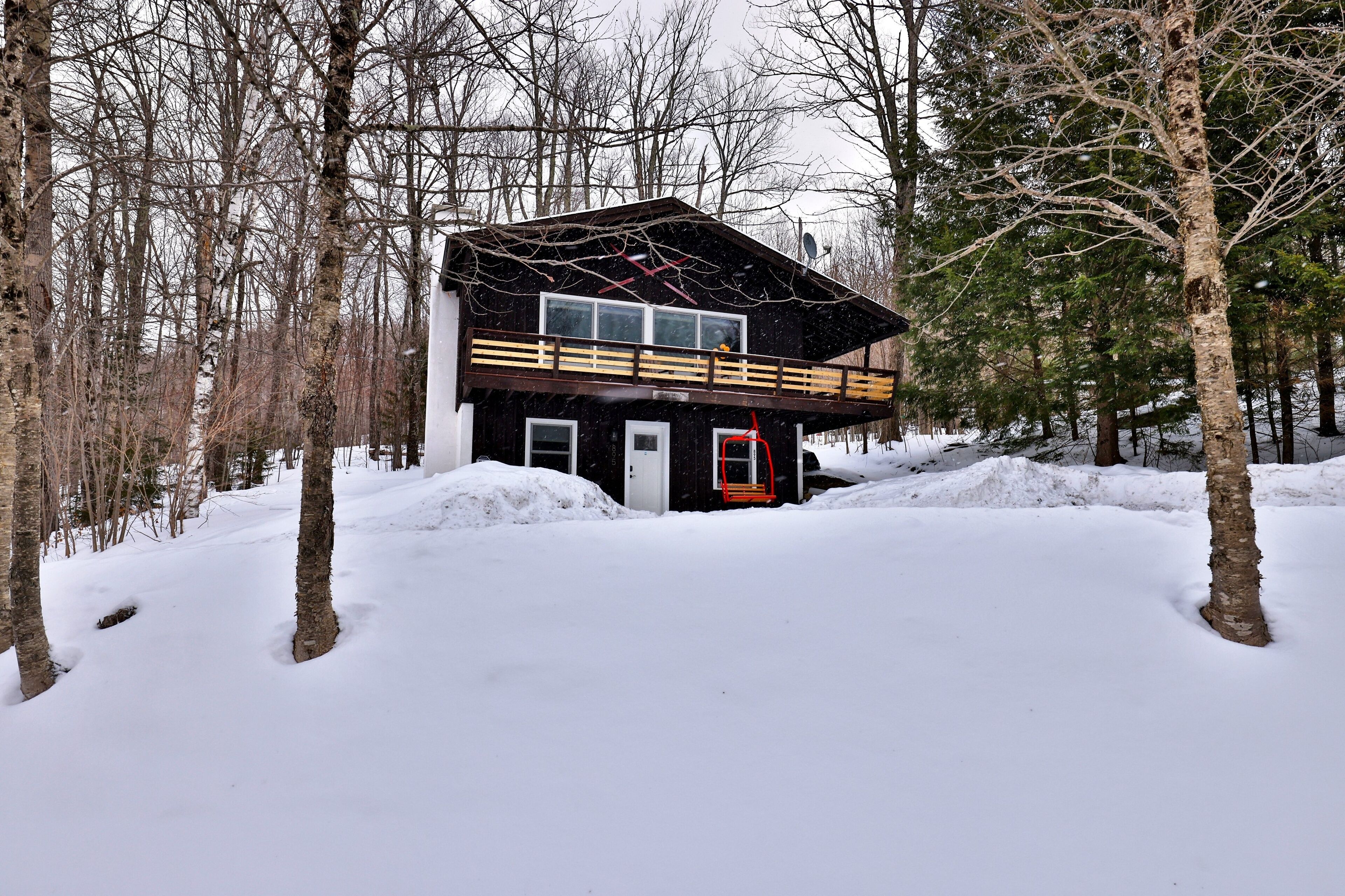 A cabin with a wooden deck and a red door, surrounded by snow and trees.