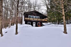 A cabin with a wooden deck and a red door, surrounded by snow and trees. - Shreadquarters 3 Bedroom Home (Killington)