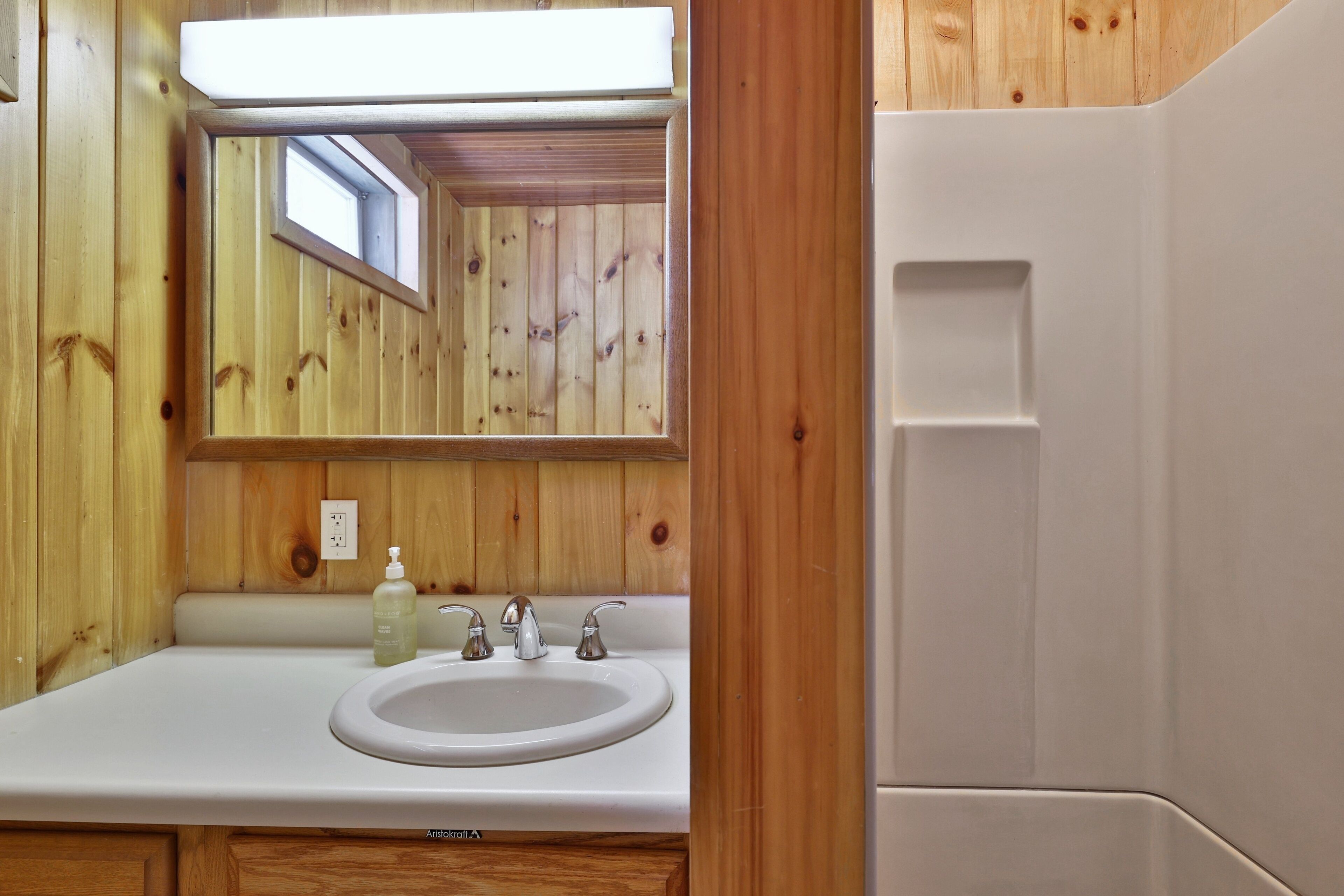 A bathroom with wooden walls, a white sink, and a mirror.