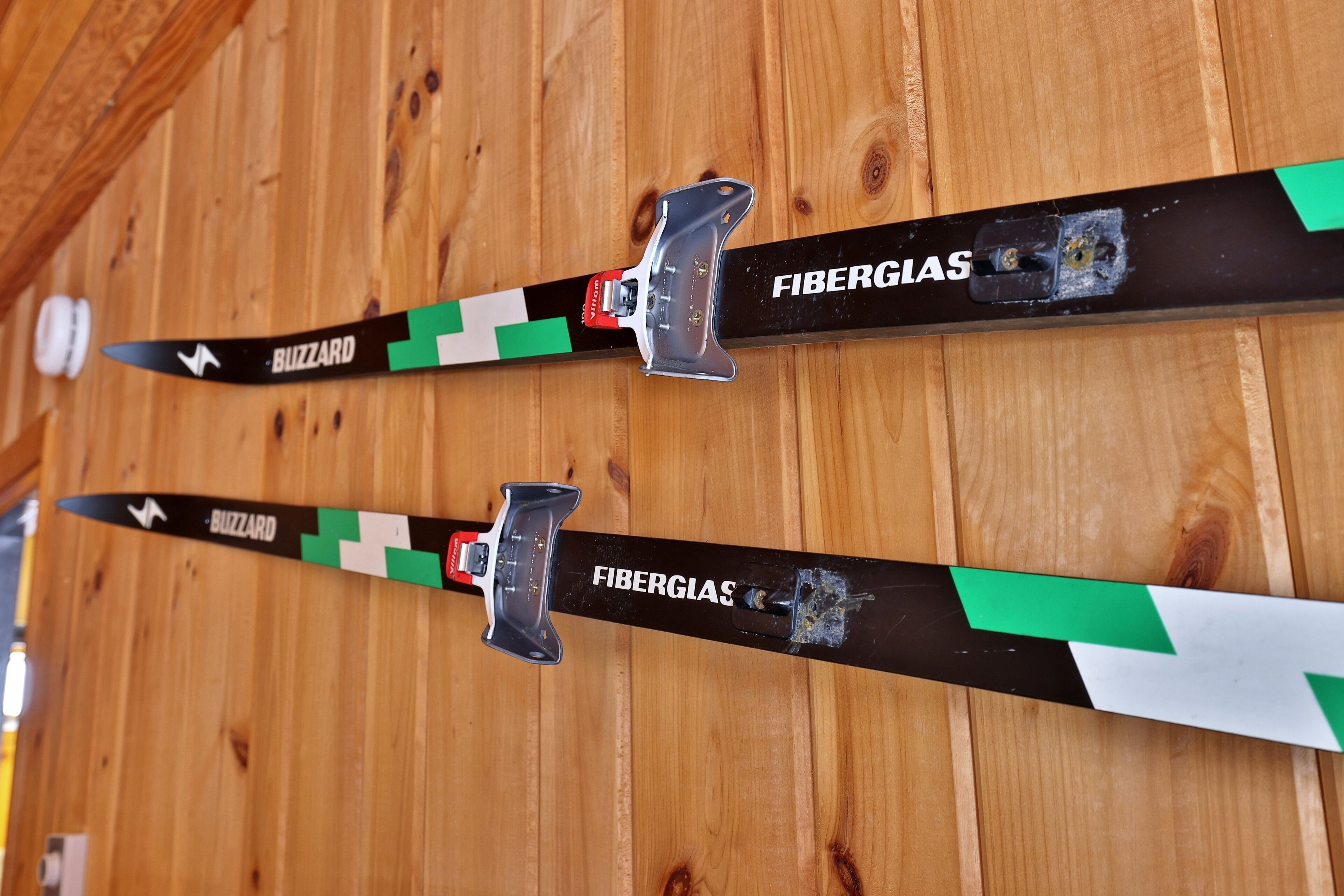 Two pairs of skis with 'Buzzard' and 'Fiberglas' branding, mounted on a wooden wall.