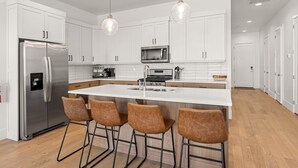 A modern kitchen with white cabinets, stainless steel appliances, a large island with bar stools, and pendant lighting. - Villa #24 At Bloomington Country Club 4 Bedroom Townhouse (St. George)