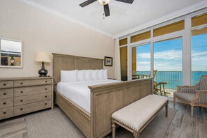A hotel room with a bed, a dresser, a bench, a chair, a ceiling fan, and a balcony with a view of the ocean. - Phoenix Gulf Towers 1105 4 Bedroom Condo (Orange Beach)
