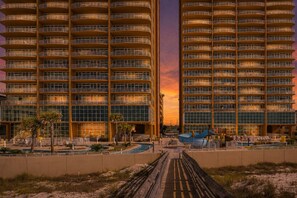 A high-rise hotel with multiple balconies, a swimming pool, and a boardwalk leading to a beach. - Phoenix Gulf Towers 1105 4 Bedroom Condo (Orange Beach)